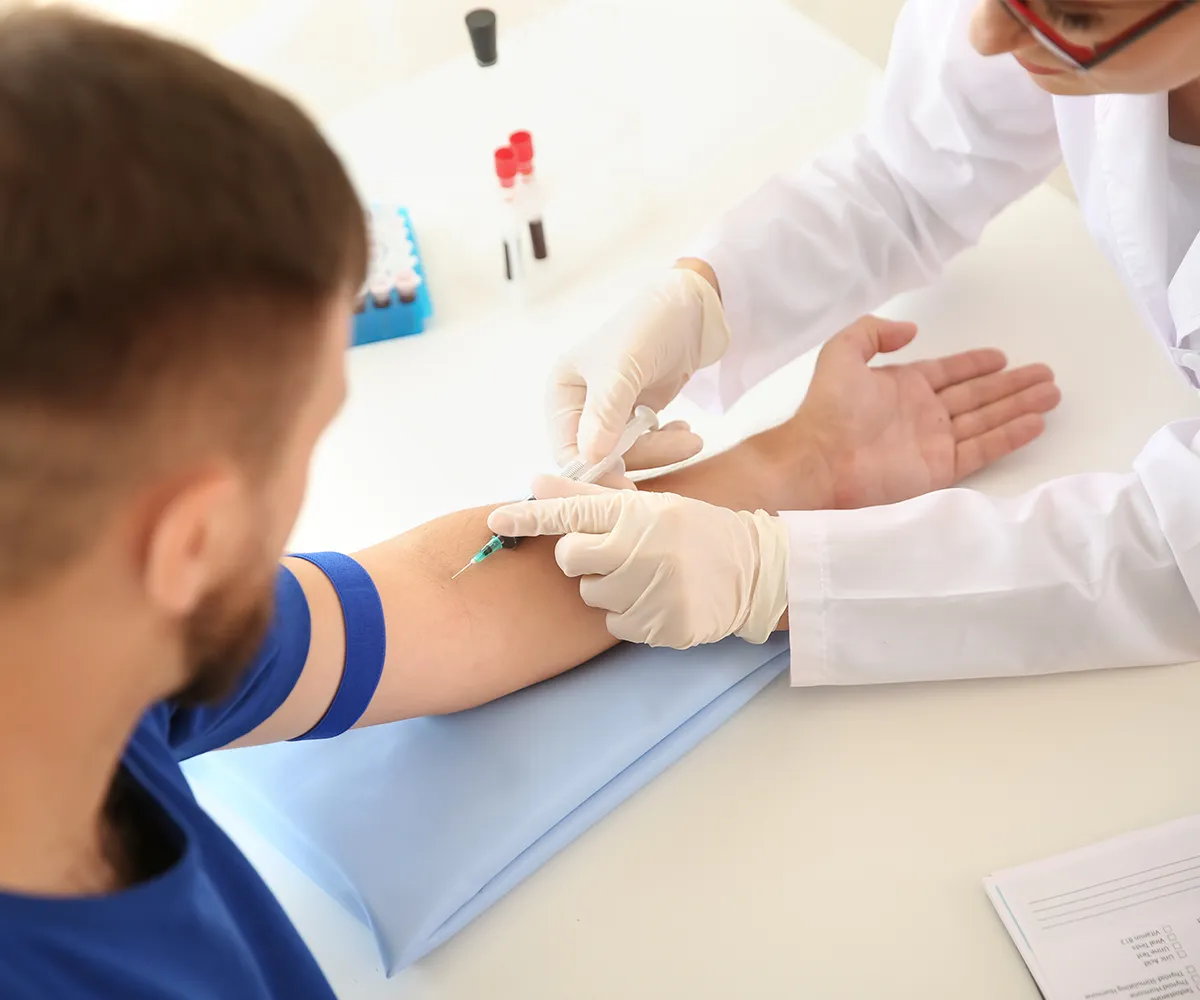 Eine weibliche medizinische Fachkraft nimmt bei einer männlichen Person am linken Arm Blut ab