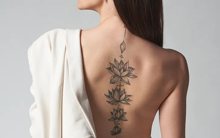 Eine weibliche Person mit vielen Blütentattoos auf der Wirbelsäule