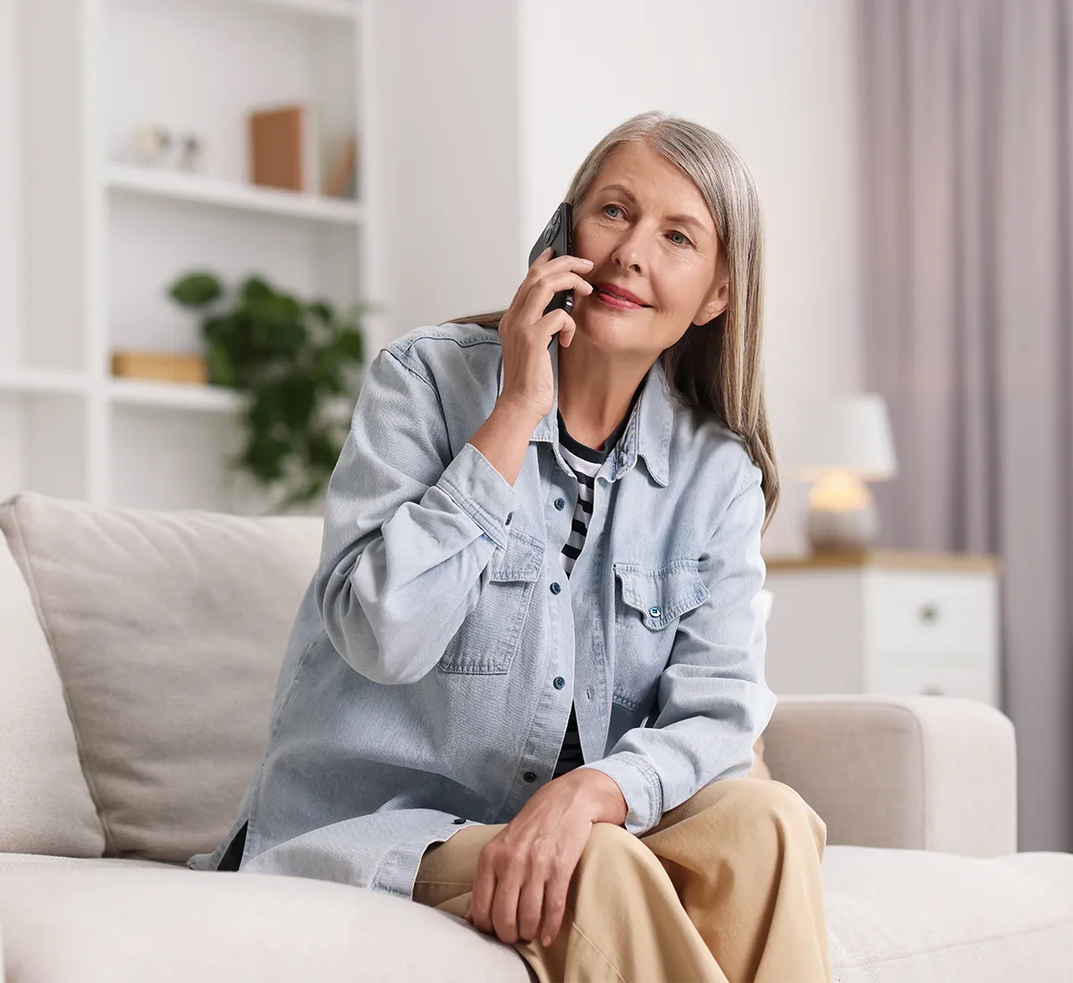 Eine ältere weibliche Person sitzt auf einer Couch mit einem Handy am Ohr in einem hellen Raum