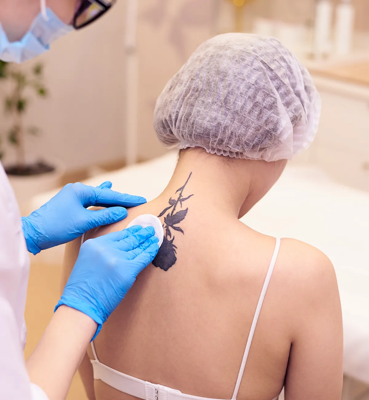 Ein medizinisches Personal reibt den tätowierten Nackenbereich einer Person mit einem Wattepad ein